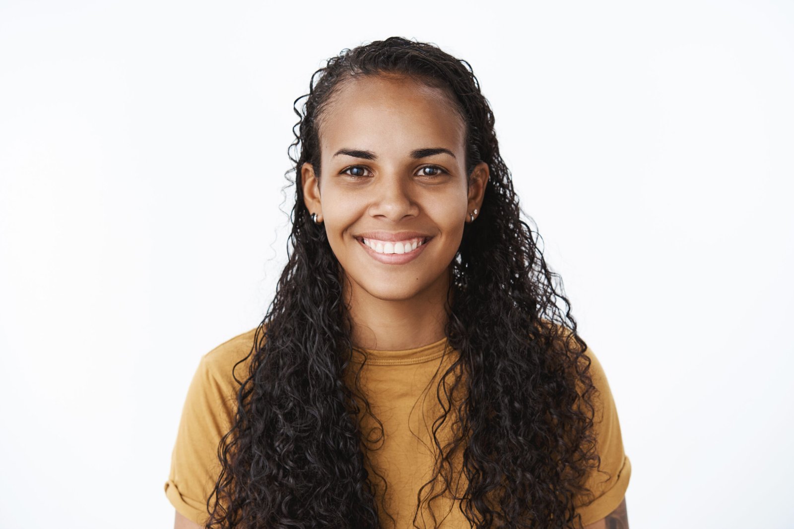 Clsose-up shot of joyful good-looking friendly african-american woman with long curly hair and white broad smile gazing at camera fulfilled and satisfied having great mood feeling happy over gray wall.